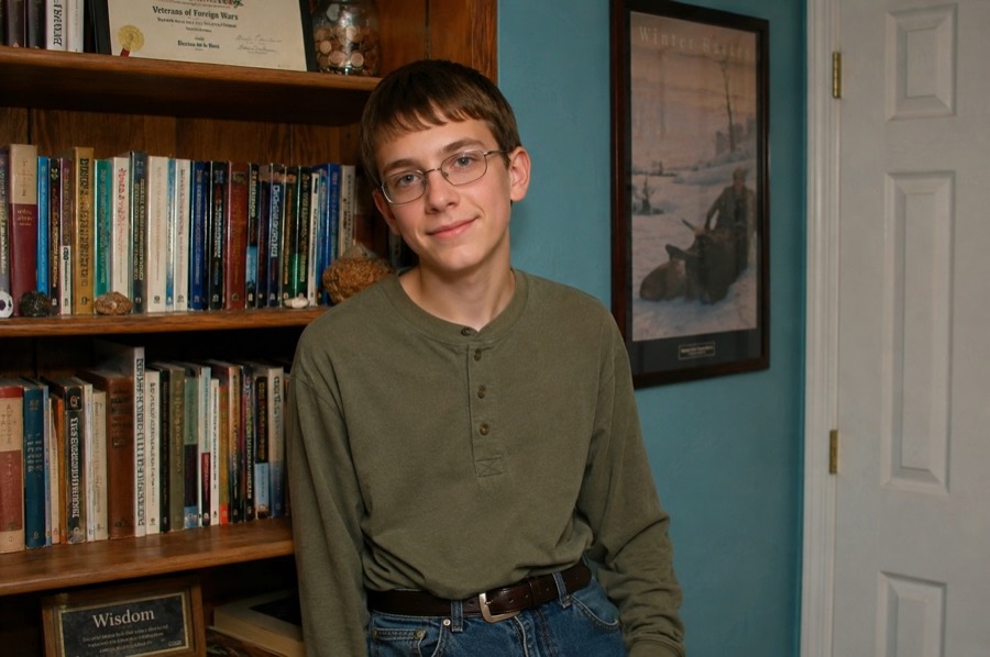 Jedidiah: a bespectacled young man in a green henley, standing
                in front of a bookshelf, unsmiling in a way that suggests he has
                already found your verse.